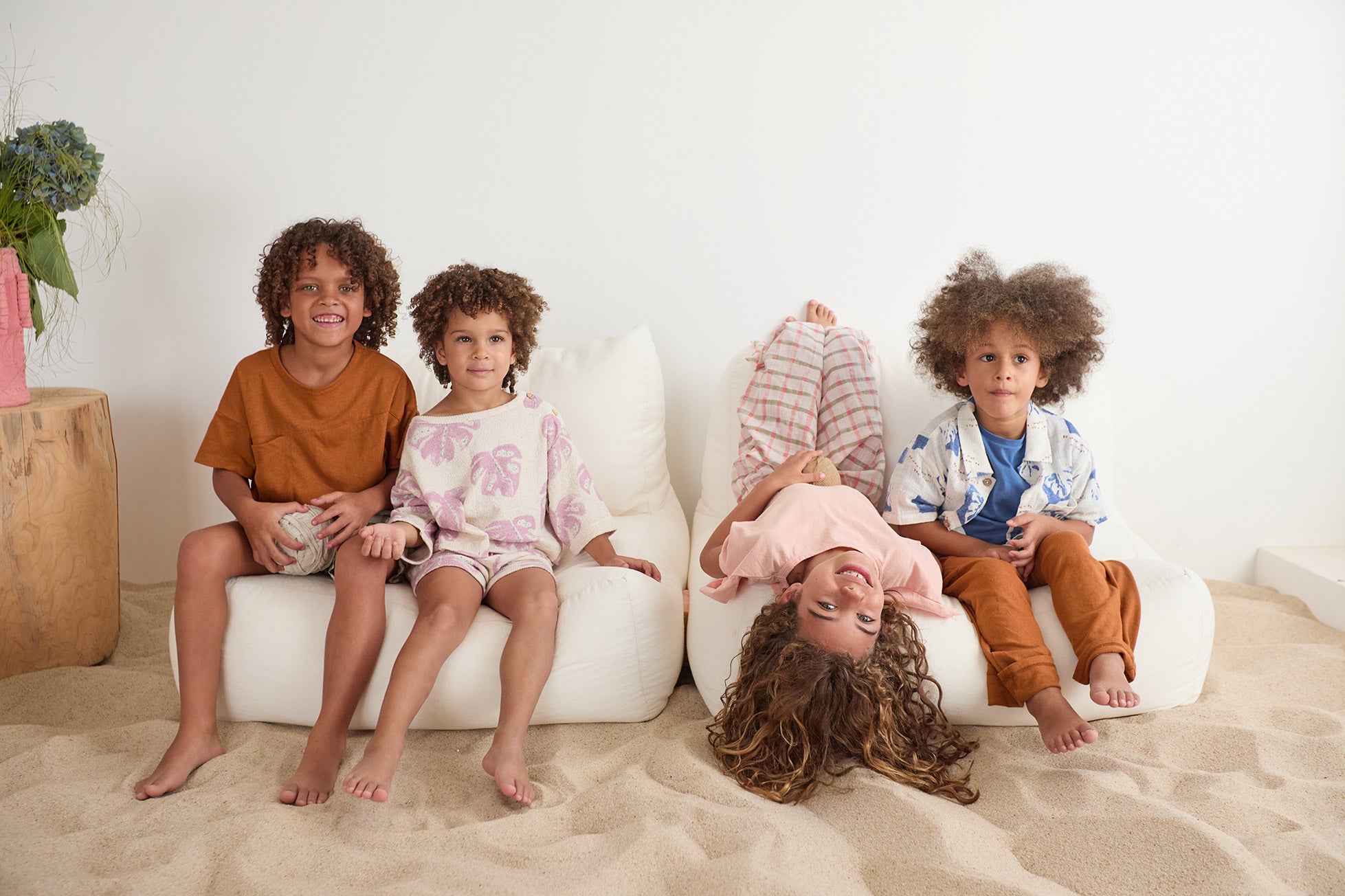 cuatro niños sentados en 2 sofas en la arena vistiendo outfits de la marca Play Up