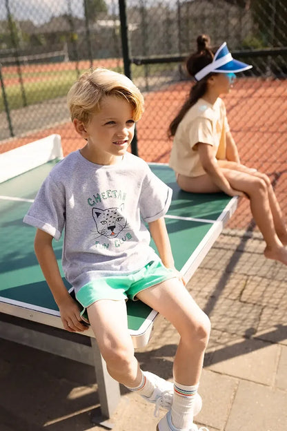 Niño sentado con camiseta gris de guepardo Cheetah Fun Club.