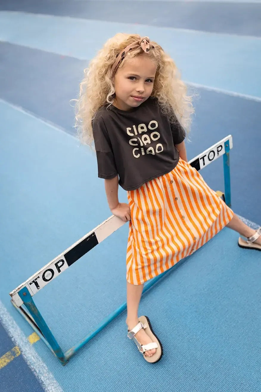 Niña con falda midi de rayas naranjas y camiseta negra Ciao.