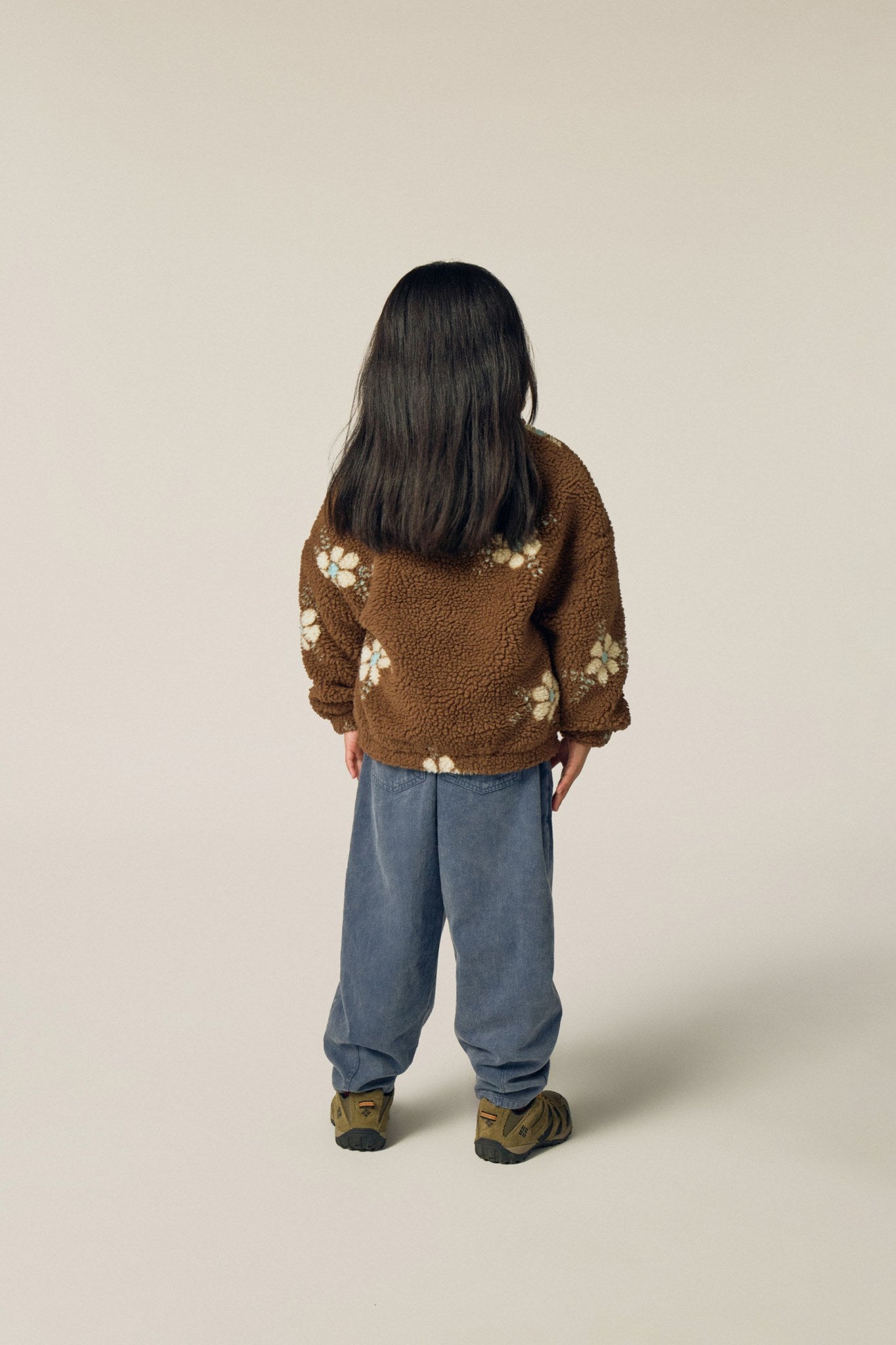 Niña de espaldas con la chaqueta marrón de flores.
