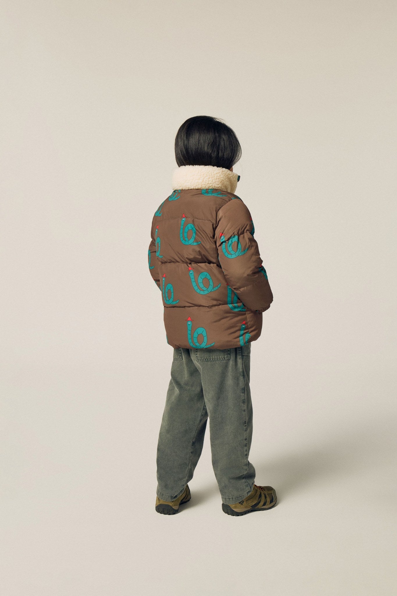 Niña de espaldas con la chaqueta marrón de serpientes.