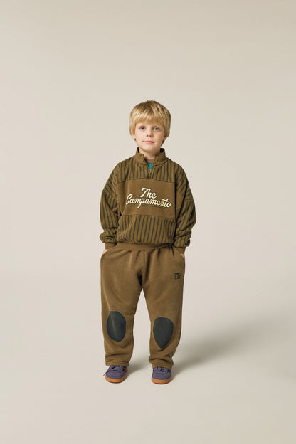 Niño posando de frente con pantalón marrón y rodilleras.