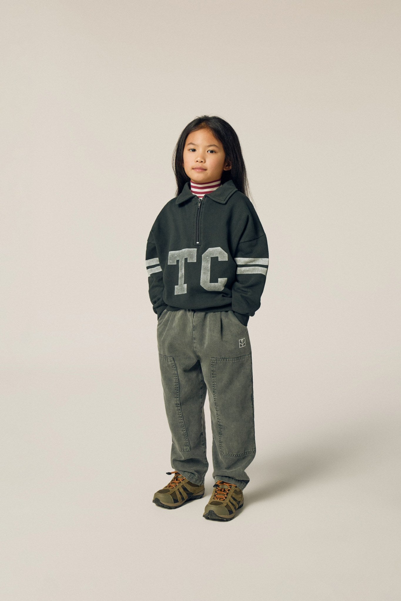 Niña posando de frente con la sudadera gris de letras TC.