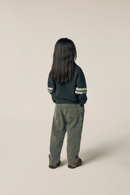 Niña de espaldas con la sudadera gris de bandas.