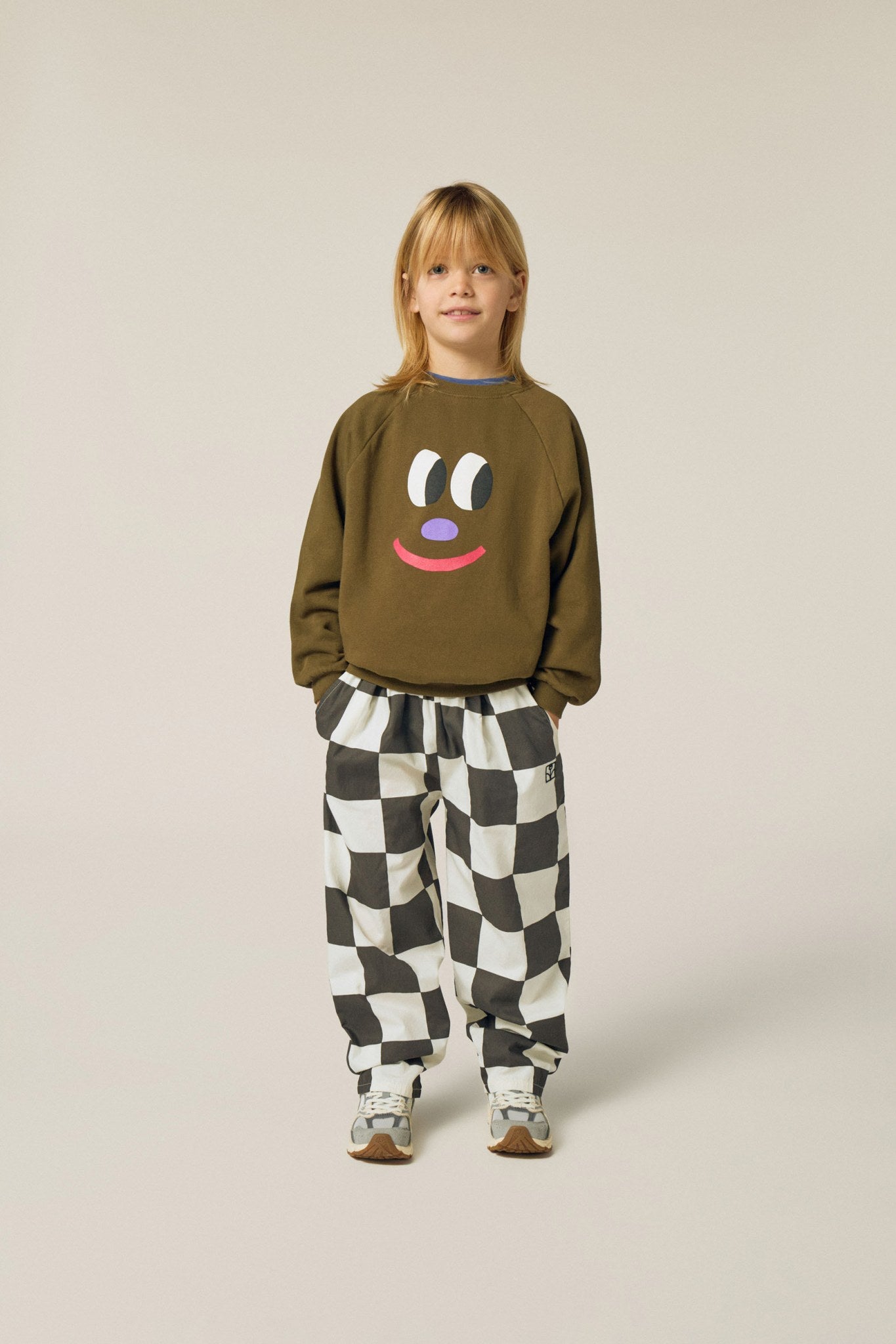 Niña posando de frente con la sudadera marrón de cara sonriente.
