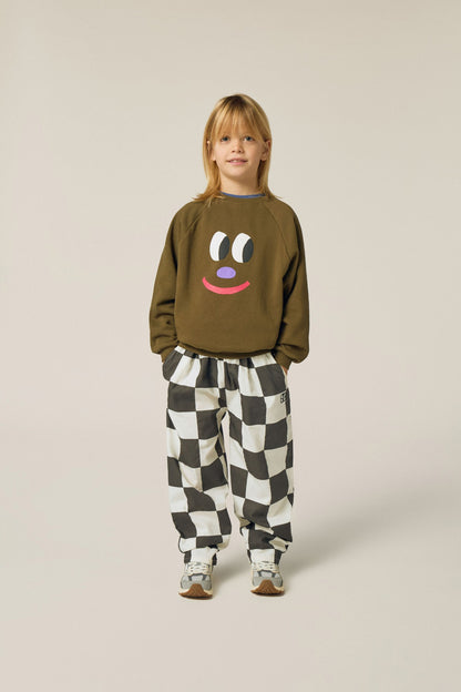 Niña posando de frente con la sudadera marrón de cara sonriente.